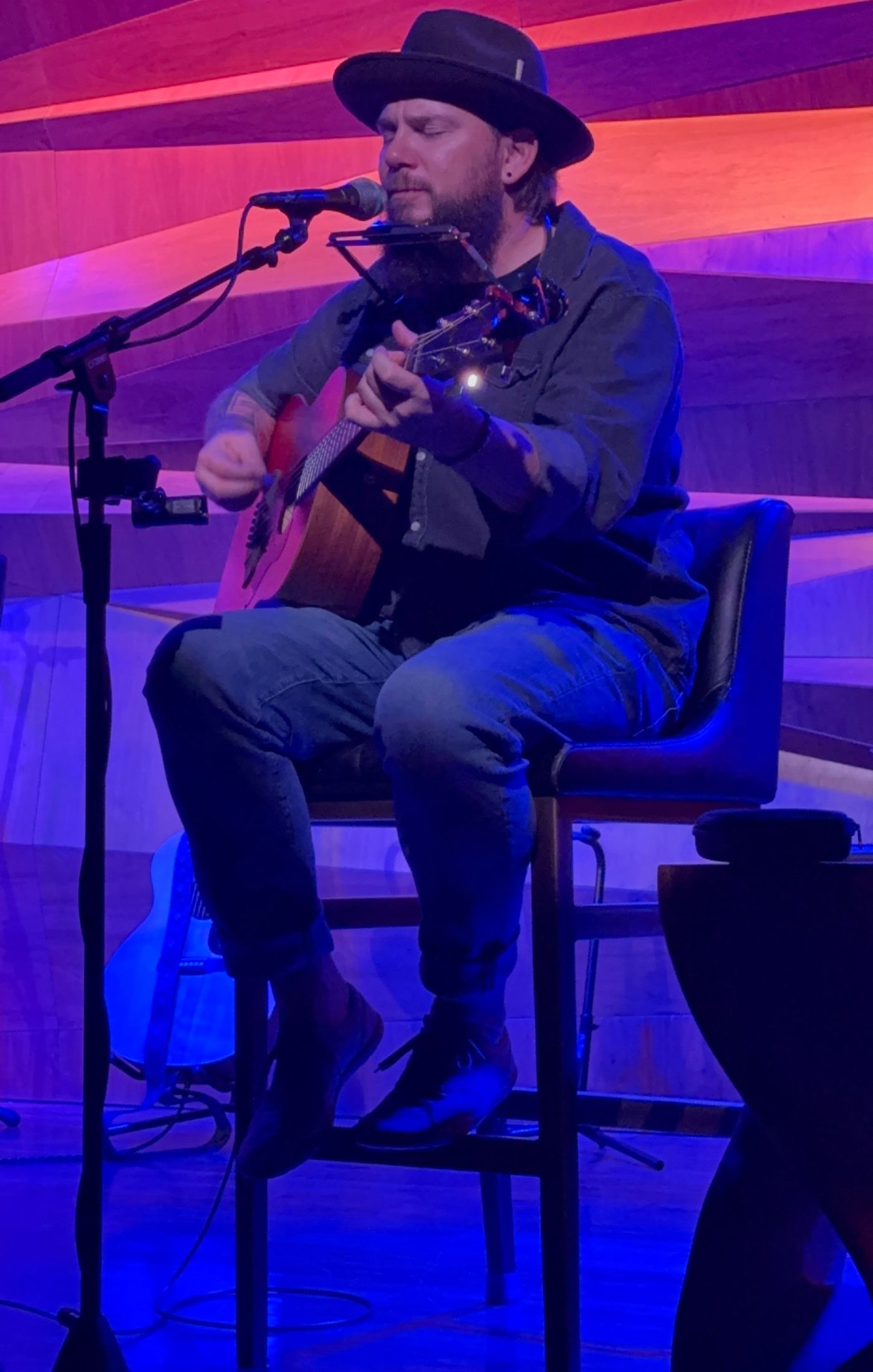 Colin Roberts performing seated with acoustic guitar and harmonica